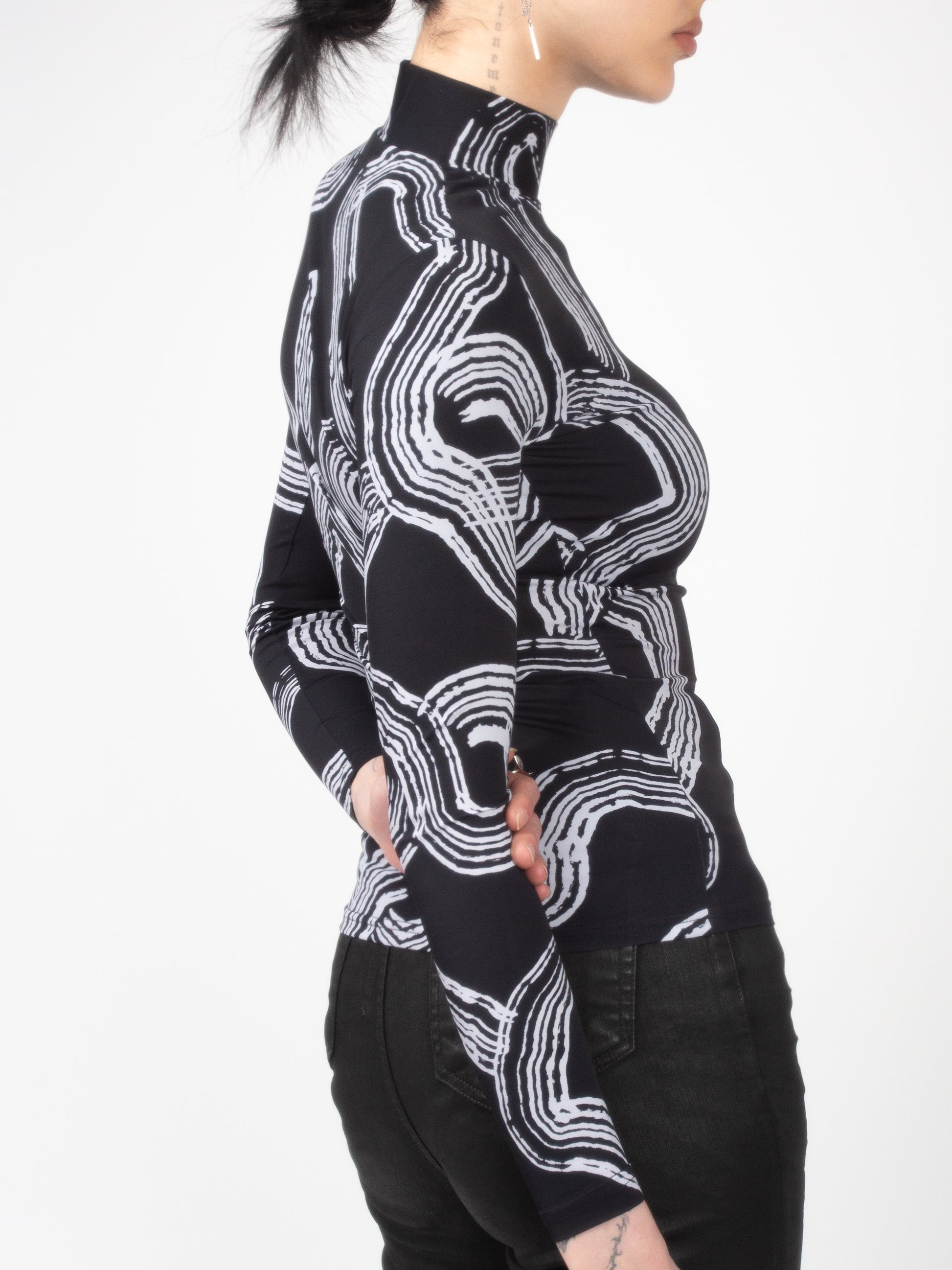 Close-up side view of female model wearing Onyx Tide bodysuit jersey top black and white ocean print on jersey fabric by VinöniV / VinoniV featuring fluid, water-inspired design.